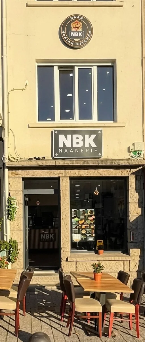 La façade du NBK Bain-de-Bretagne : l’enseigne ronde NBK, l’enseigne NBK Naanerie au-dessus de la vitrine, et la terrasse sur la place