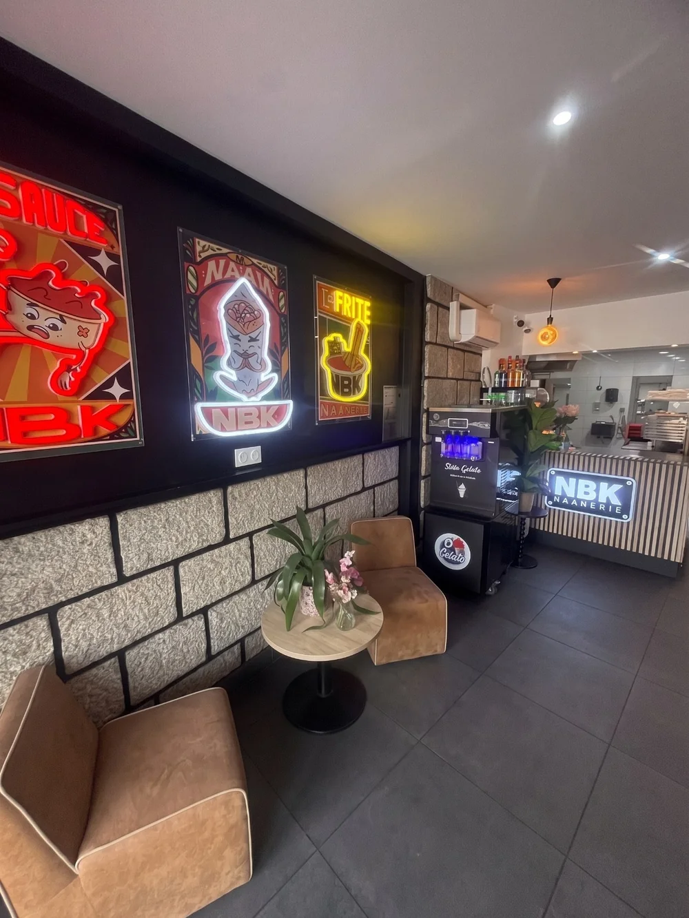 La salle du NBK Bain-de-Bretagne : les affiches NBK de la sauce, du naan et de la frite en néon, deux fauteuils, et le comptoir au fond