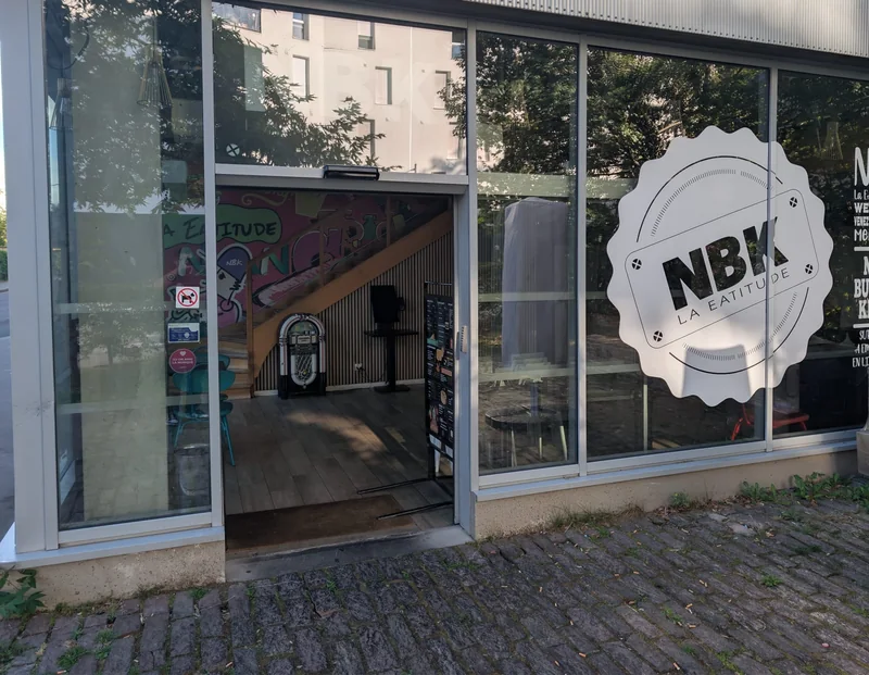 L’entrée du NBK Rennes La Courrouze, porte ouverte : l’enseigne ronde NBK sur la vitre, et à l’intérieur un juke-box devant la fresque graffée de la marque