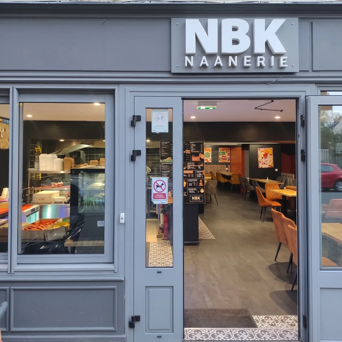 La devanture grise du NBK Redon et son enseigne NBK Naanerie : la porte ouverte sur la salle aux chaises orange, et la cuisine derrière la vitrine