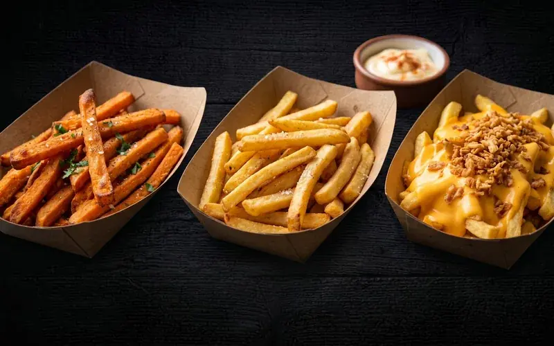 Trois barquettes de frites NBK : frites de patate douce, frites classiques, et cheezy frites nappées de cheddar et d’oignons frits