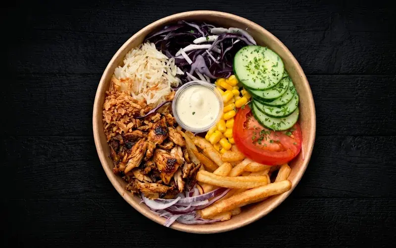 Un bowl NBK vu de dessus : poulet grillé, riz, chou rouge, maïs, concombre, tomate, frites, oignons frits et sauce blanche