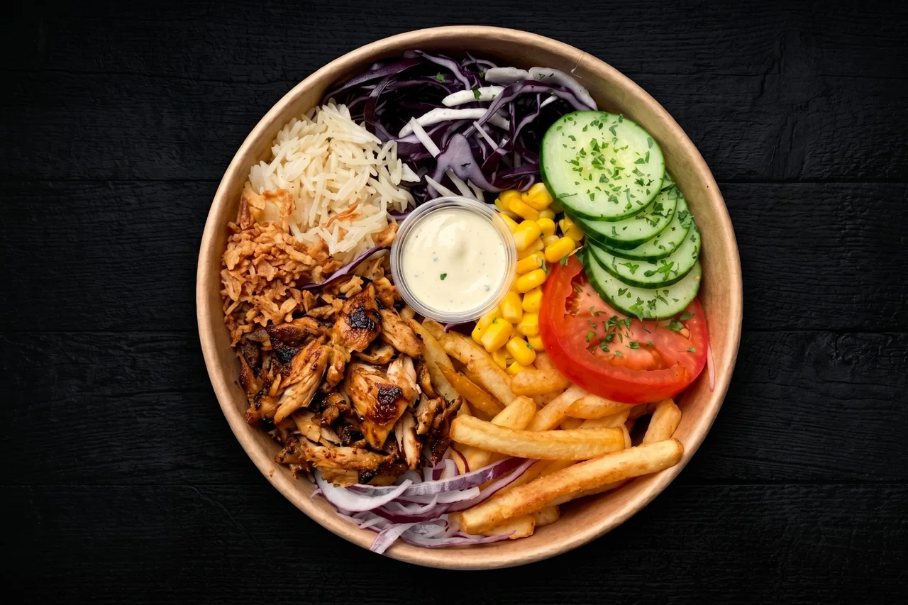 Un bowl NBK vu de dessus : poulet grillé, riz, chou rouge, maïs, concombre, tomate, frites, oignons frits et sauce blanche