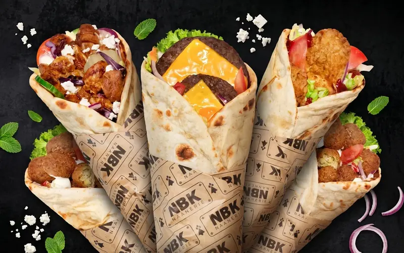 Cinq cheese naans NBK dans leur papier siglé, sur fond noir : kebab et féta, steak et cheddar, poulet croustillant et falafels