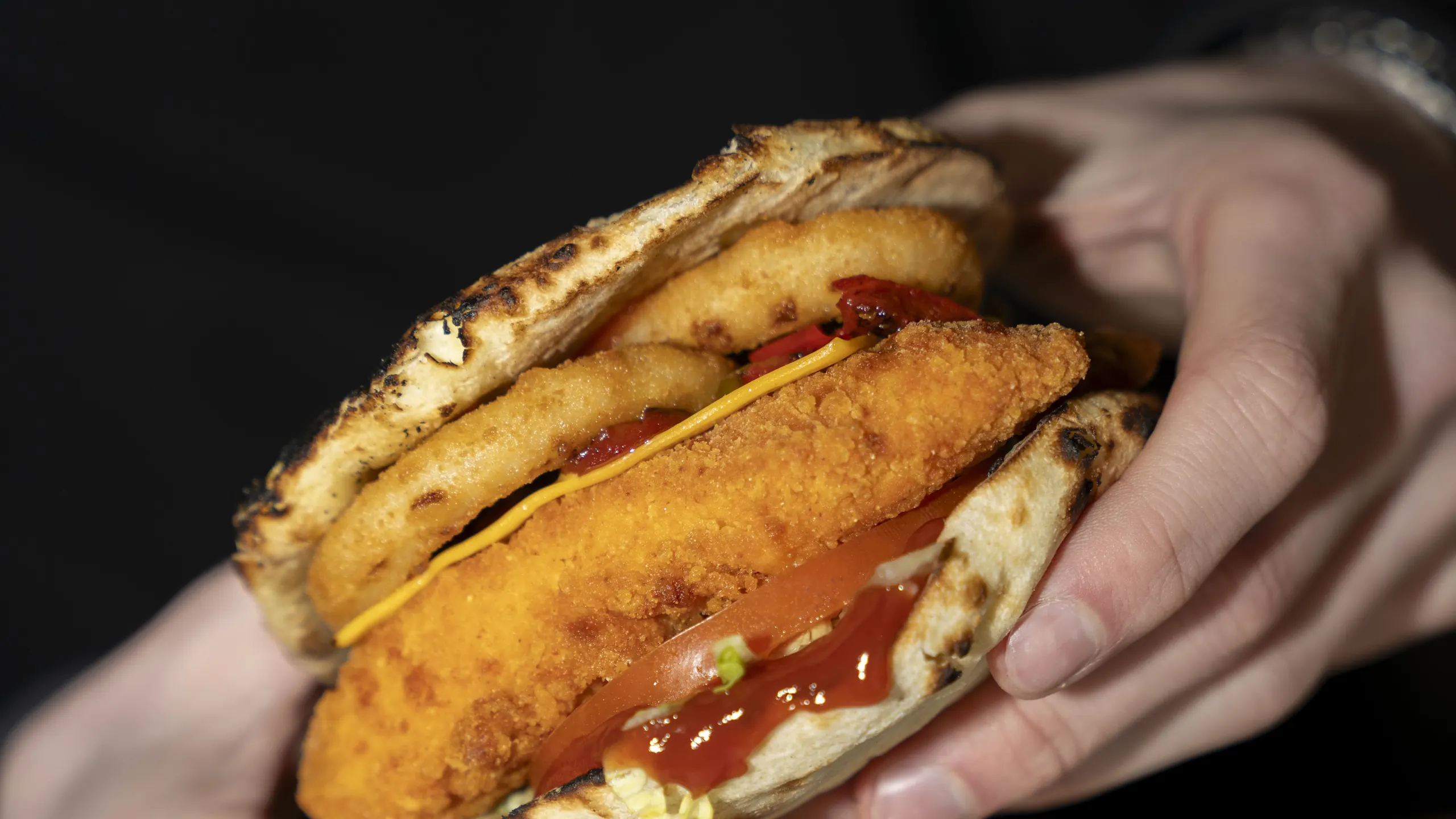 Deux mains tiennent un naan burger NBK garni de poulet croustillant, tomate et cheddar