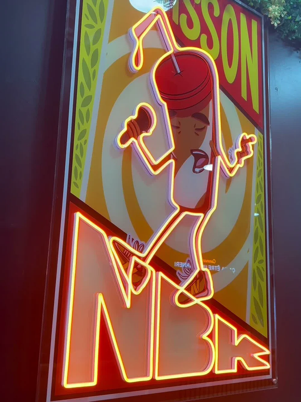 L’enseigne néon NBK orange qui éclaire une affiche illustrée, dans la salle du restaurant