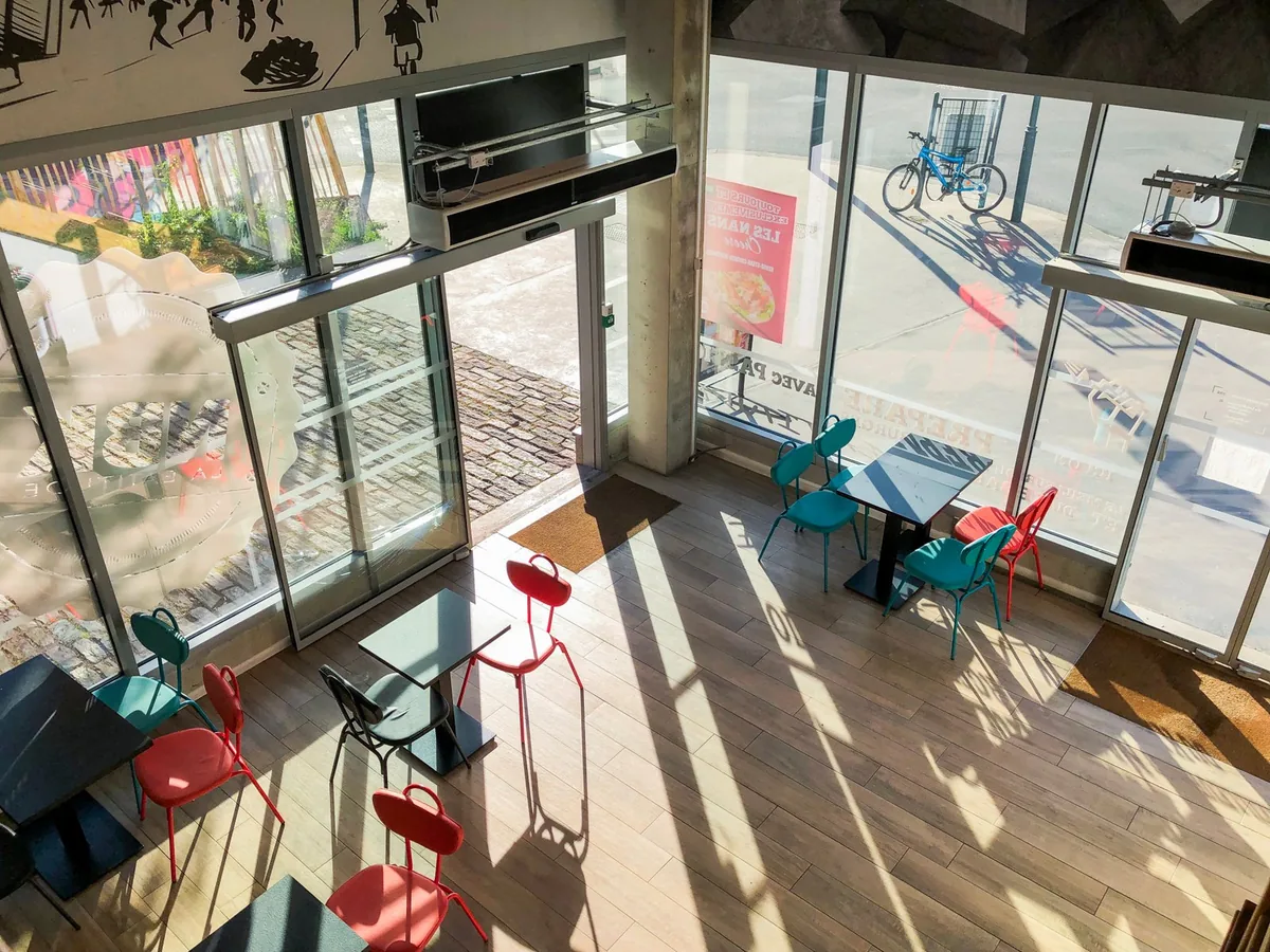 L’entrée du NBK Rennes La Courrouze vue de la mezzanine : de grandes baies vitrées, des tables et des chaises bleues et rouges