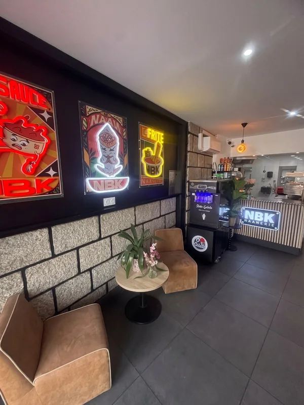 La salle du NBK Bain-de-Bretagne : les affiches NBK de la sauce, du naan et de la frite en néon, deux fauteuils, et le comptoir au fond