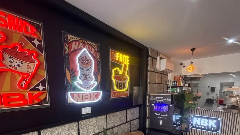 La salle du NBK Bain-de-Bretagne : les affiches NBK de la sauce, du naan et de la frite en néon, deux fauteuils, et le comptoir au fond