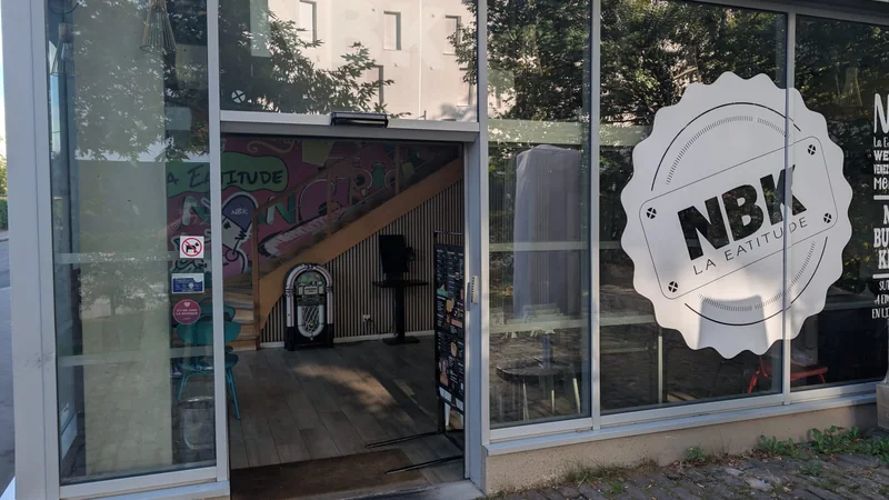L’entrée du NBK Rennes La Courrouze, porte ouverte : l’enseigne ronde NBK sur la vitre, et à l’intérieur un juke-box devant la fresque graffée de la marque